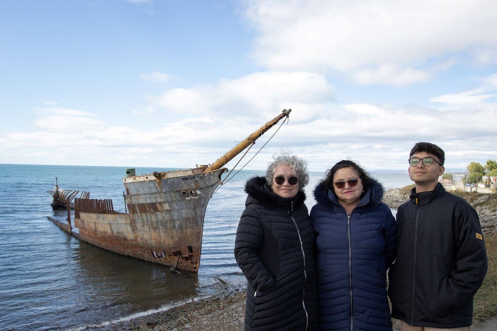 Viajeros en la costanera de Punta Arenas frente al casco de un antiguo barco varado en el Estrecho de Magallanes